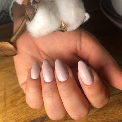 Dłoń z pomalowanymi na jasny, pudrowy róż paznokciami w kształcie migdała, dekorowana gałązką bawełny i orzechem na drewnianym tle.