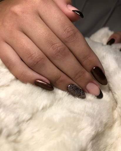 Dłoń z ciemnobrązowym manicure hybrydowym, jeden paznokieć z wzorem mandali, na puszystym białym tle.