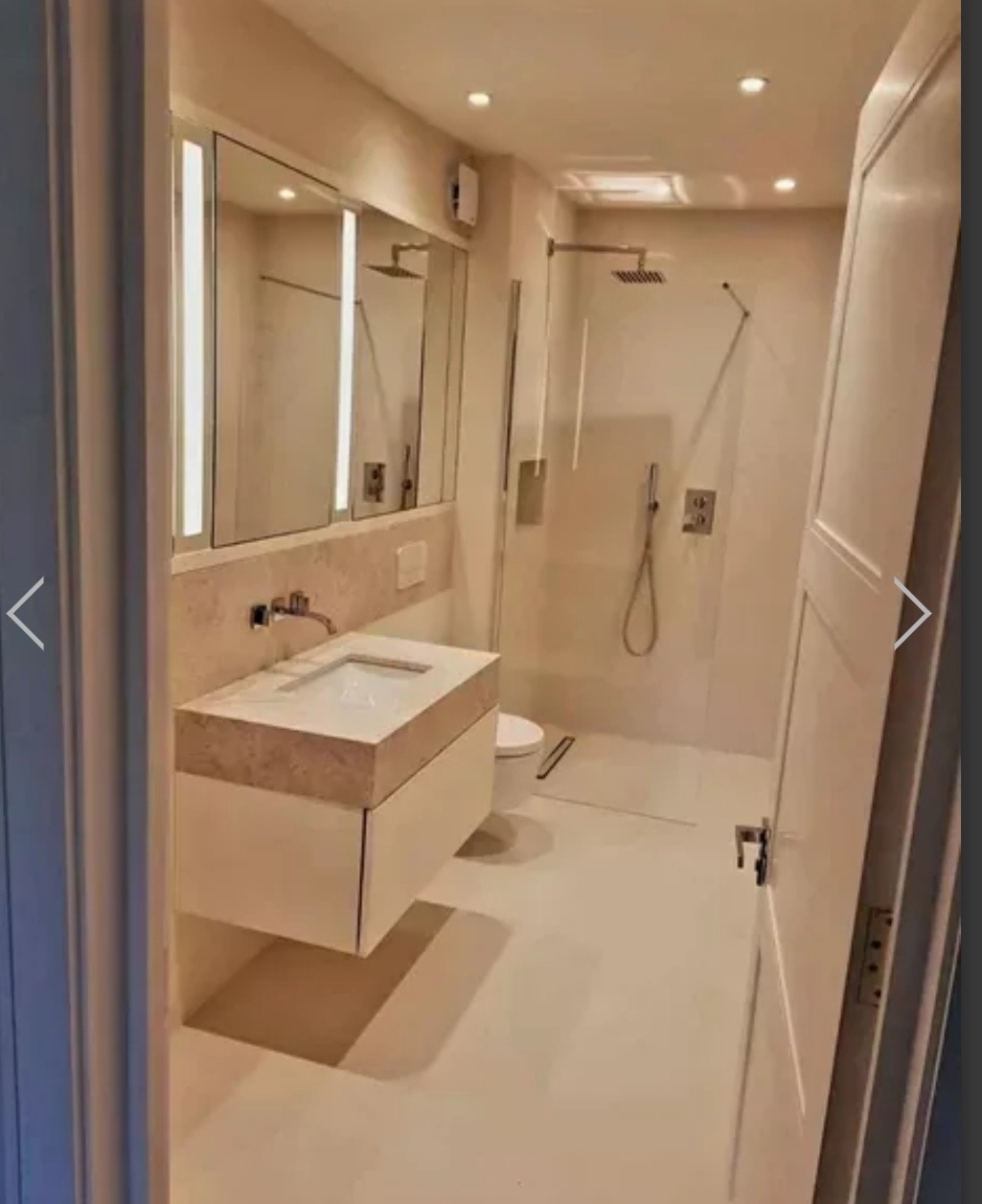 Nowoczesna łazienka z podwieszaną umywalką z blatem imitującym kamień, kabiną prysznicową typu walk-in i subtelnym oświetleniem punktowym.