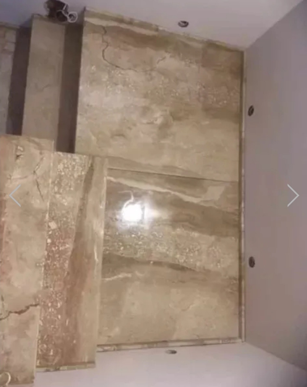 Wnętrze domu w trakcie wykańczania, ściany i schody wyłożone płytami imitującymi marmur w odcieniach beżu i brązu, widoczne otwory na oświetlenie w suficie.