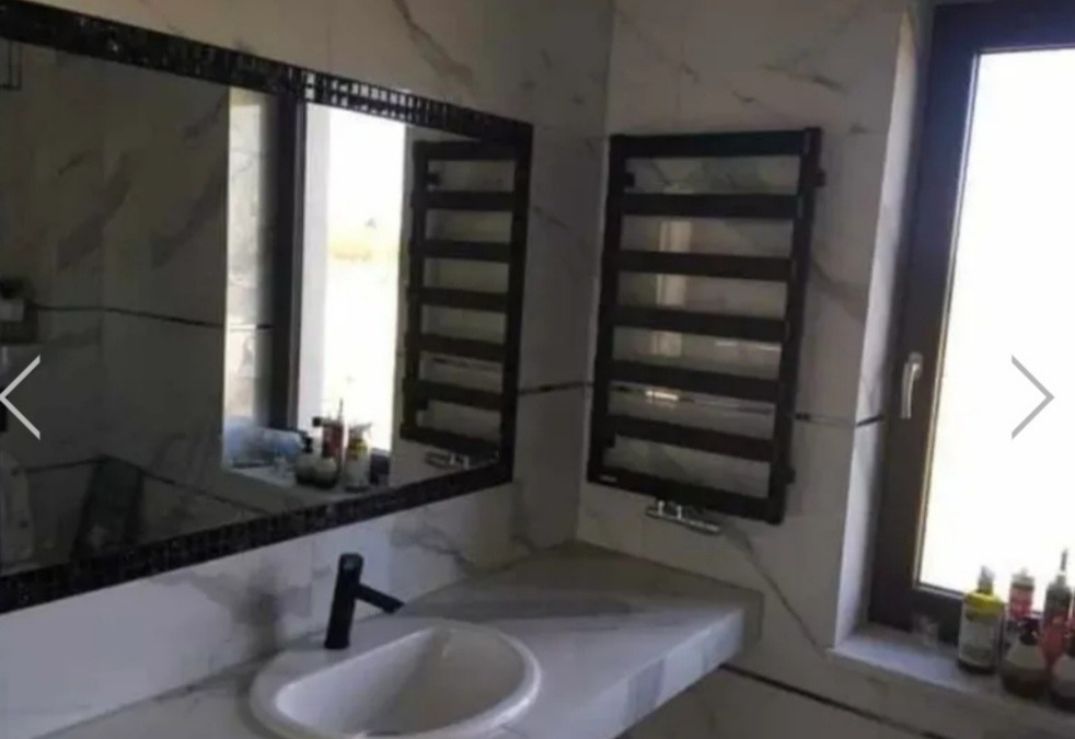 Nowoczesna łazienka z marmurowymi płytkami, czarną armaturą, grzejnikiem drabinkowym i dużym lustrem z ozdobną ramą.