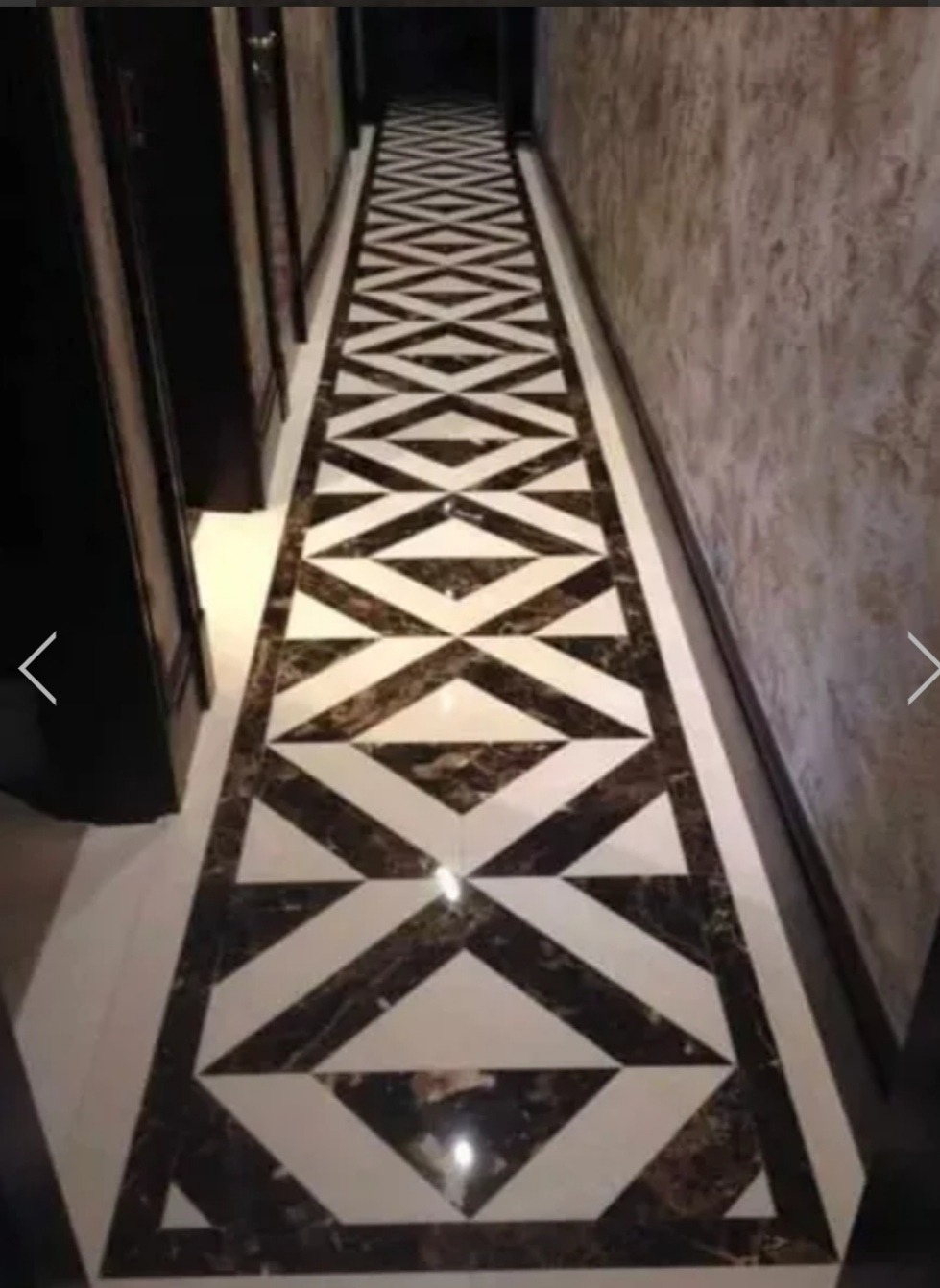 Długi korytarz z podłogą z ciemnego marmuru z białymi wstawkami tworzącymi geometryczny wzór rombów i trójkątów.