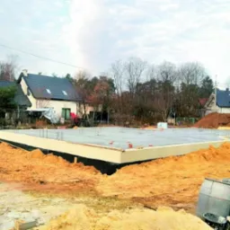 Zabezpieczony fundament z izolacją pionową i poziomą w Szymbarku, widoczne zbrojenia i przygotowany pod wylewkę, w tle zabudowa jednorodzinna.