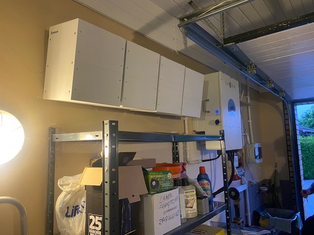 Montaż modułowego systemu magazynowania energii Breeze w garażu, widoczny również inwerter Solis, metalowy regał z narzędziami i akcesoriami.