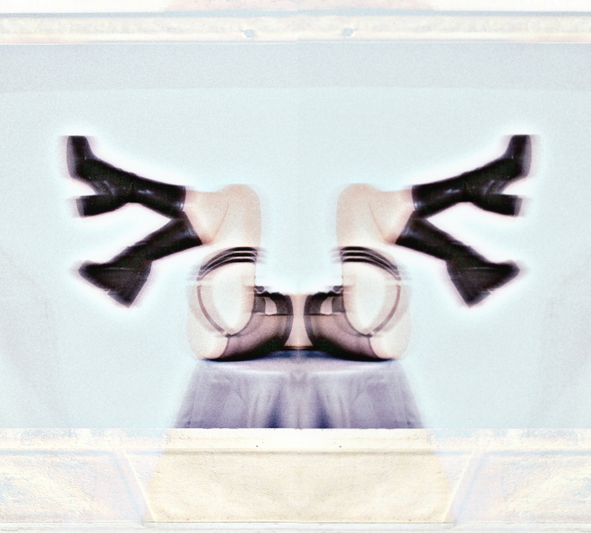 Abstrakcyjne, symetryczne ujęcie nóg w czarnych kozakach na obcasie, z efektem rozmycia ruchu, umieszczonych na blacie stołu, na rozmytym tle.