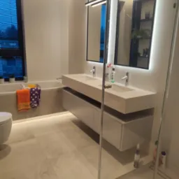 Nowoczesna łazienka z podświetlanym lustrem nad podw&oacute;jną umywalką, widok na wannę z akcesoriami i kabinę prysznicową ze szklanymi drzwiami.