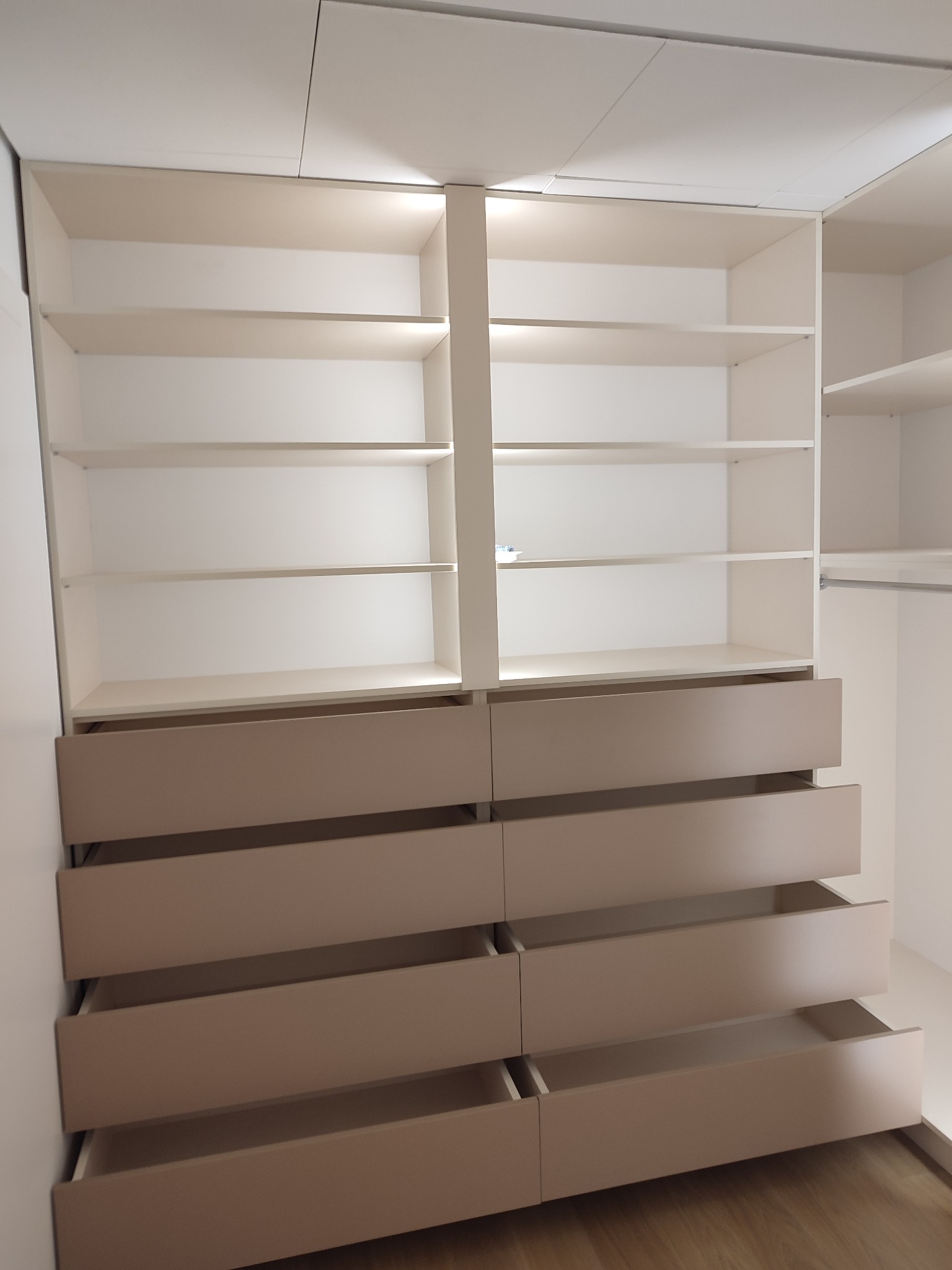 Biała szafa wnękowa z półkami i wysuwanymi szufladami w odcieniach beżu, niektóre szuflady są otwarte, ukazując wnętrze.