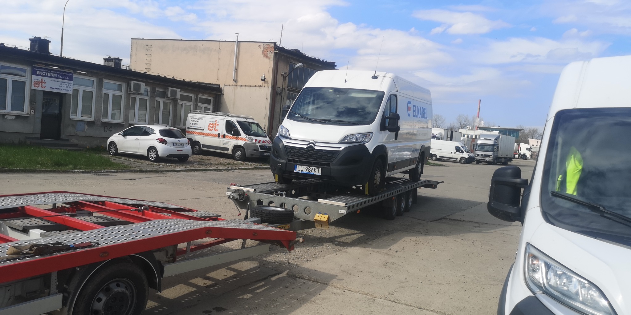 Biały Citroen Jumper z logo ELKABEL na lawecie, widoczny numer rejestracyjny LU 986KT, w tle budynek i inne pojazdy.