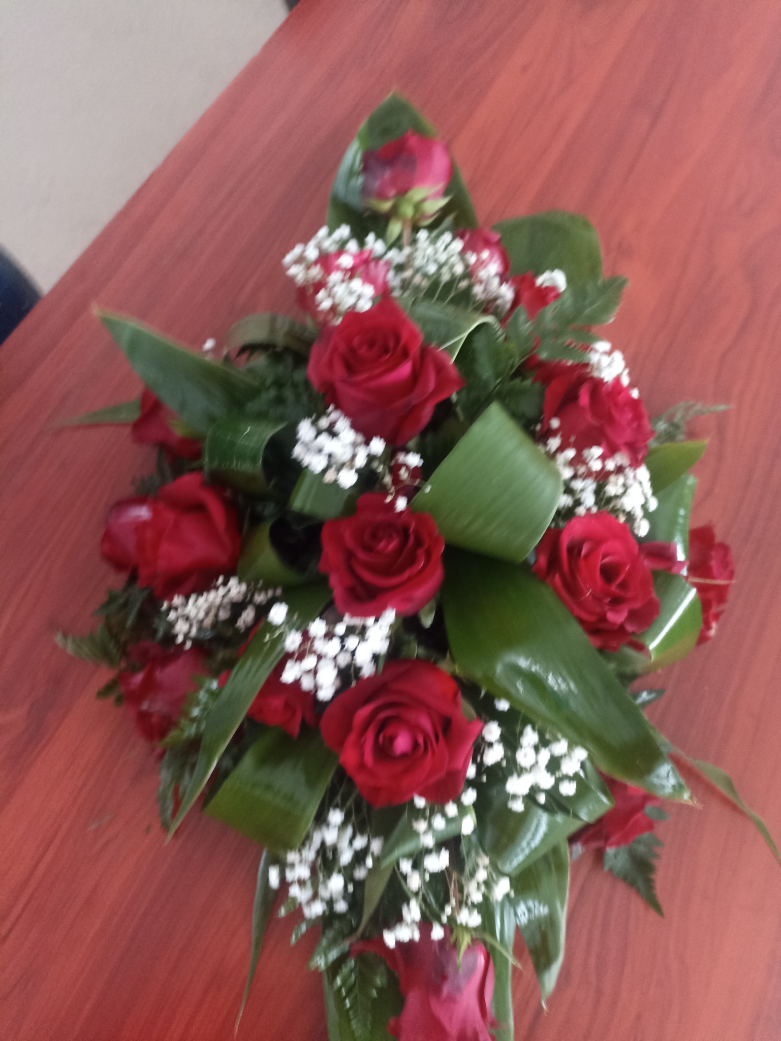 Dekoracyjny bukiet z czerwonych róż i białych gipsówek, ułożony na drewnianym stole.