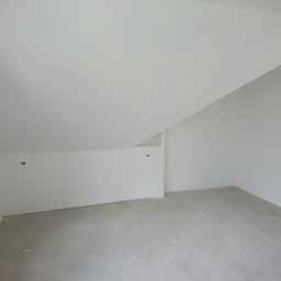 ZTM - Poddasze po szpachlowaniu i malowaniu na biało, widoczne gładkie ściany i sufit ze skosem, przygotowane do dalszych prac wykończeniowych, z widocznymi puszkami elektrycznymi.