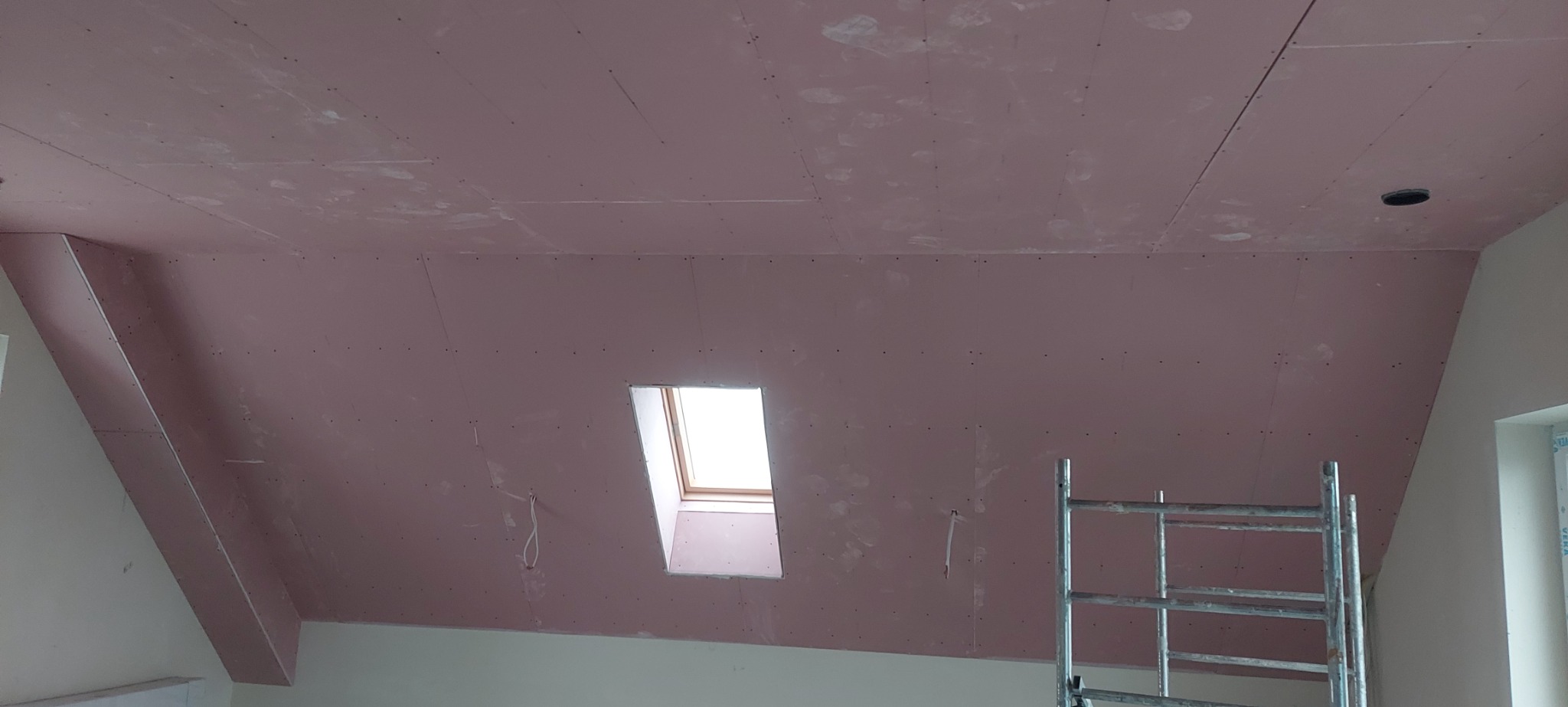 Poddasze z zamontowaną płytą karton gips, widoczne łączenia i ślady szpachlowania, okno dachowe i fragment rusztowania.