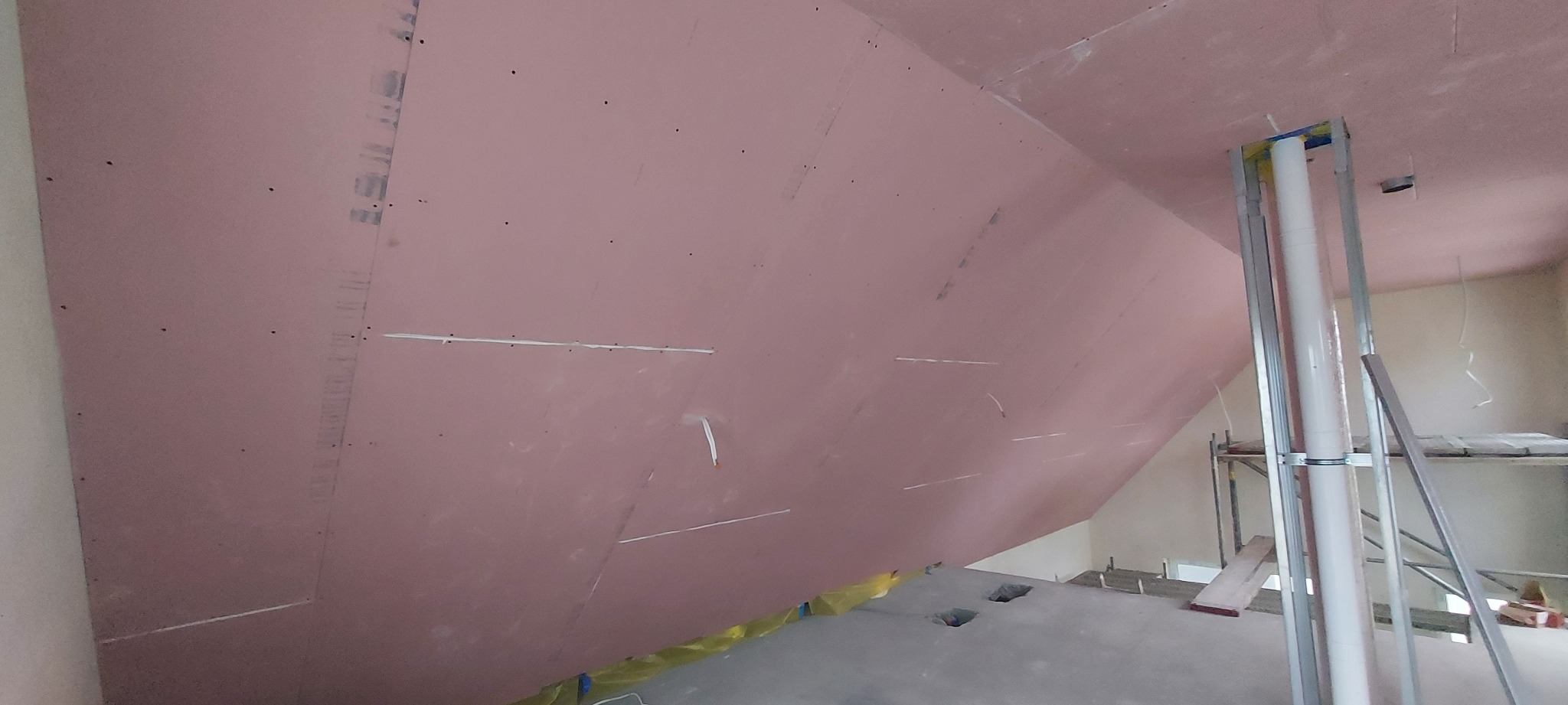 Montaż płyty karton gips na skośnym poddaszu, widoczne profile i otwory w podłodze zabezpieczone folią.