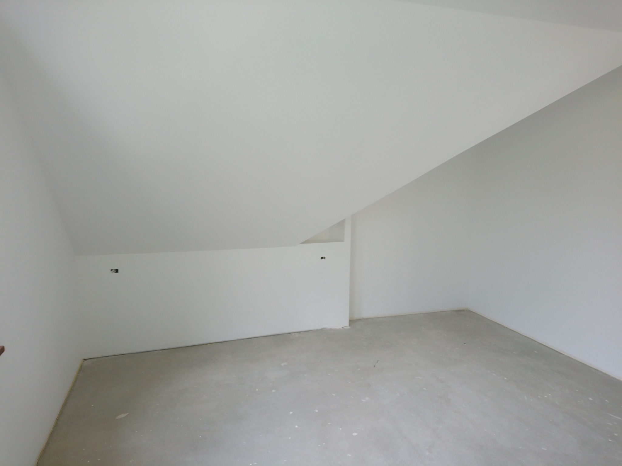 Poddasze po szpachlowaniu i malowaniu na biało, widoczne gładkie ściany i sufit ze skosem, przygotowane do dalszych prac wykończeniowych, z widocznymi puszkami elektrycznymi.