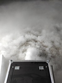 Czarna skrzynia transportowa z metalowymi okuciami, z której wydobywa się gęsta, biała mgła wypełniająca kadr.