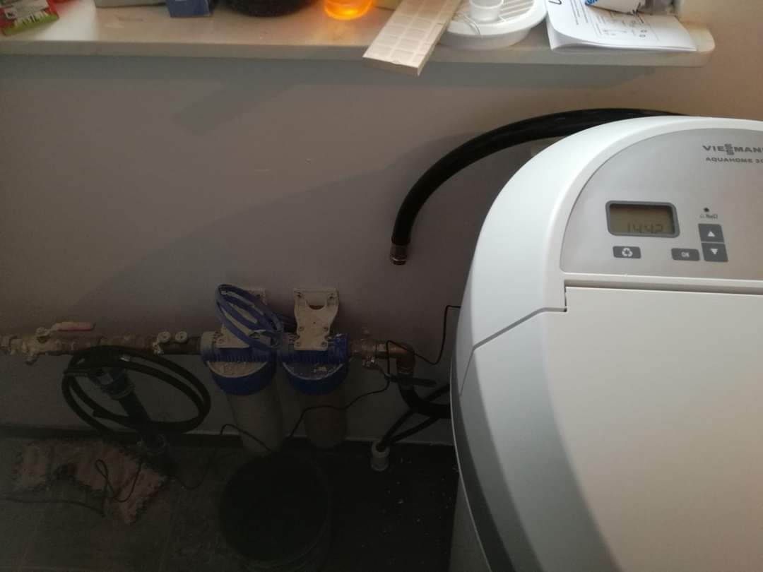 Viessmann Aquahome 20-N uzdatniacz wody z filtrami mechanicznymi podłączony do instalacji, widoczne rury i węże, na ścianie półka z akcesoriami.