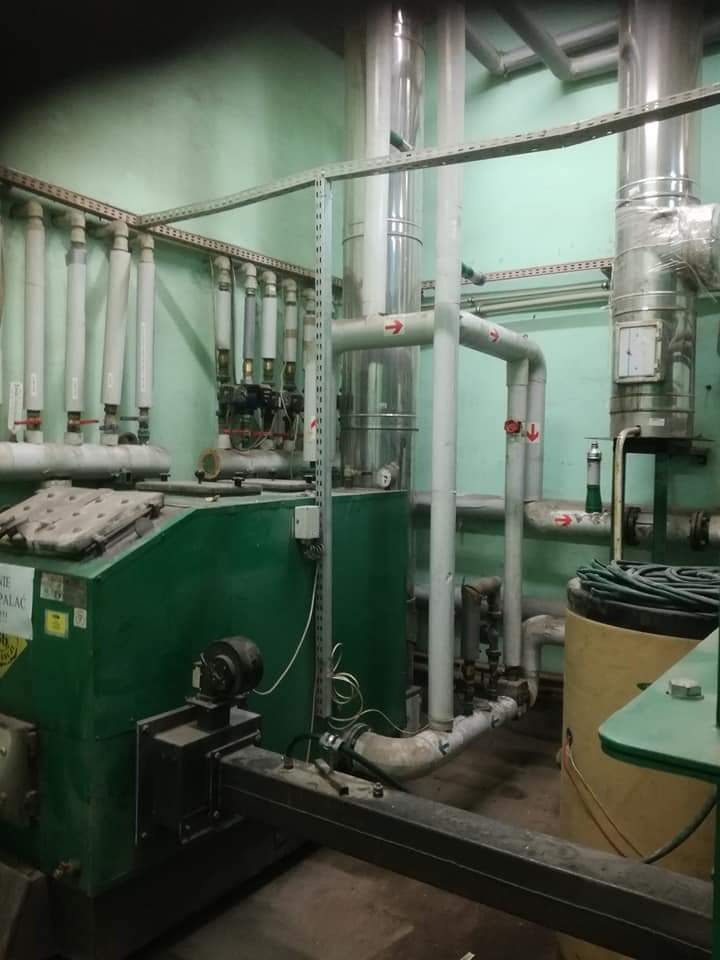 Zielony piec centralnego ogrzewania z licznymi rurami i przewodami w kotłowni o zielonych ścianach.