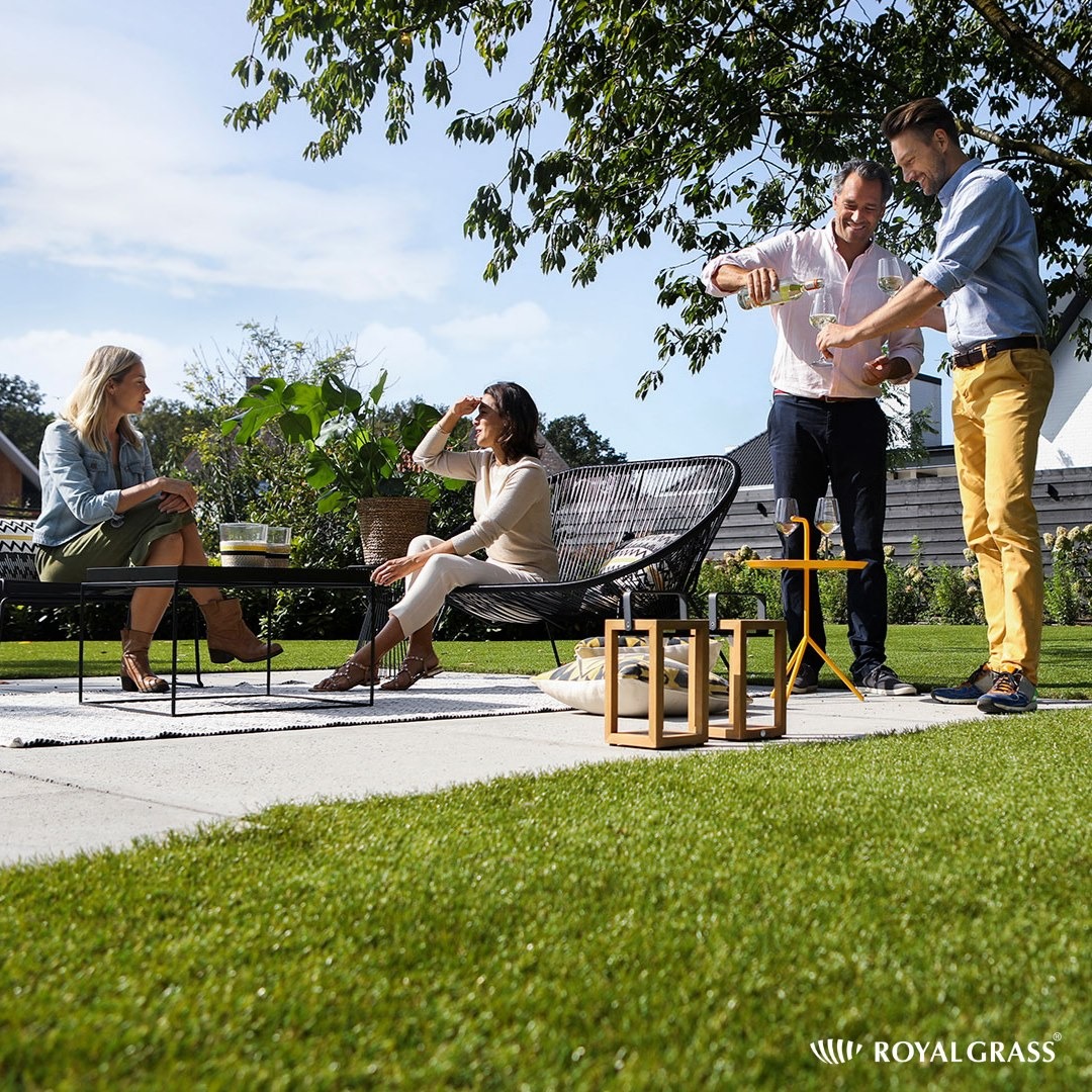 Betonowa powierzchnia tarasu z grupą osób relaksujących się w ogrodzie, mężczyzna nalewa wino do kieliszków, widoczna trawa i elementy dekoracyjne.