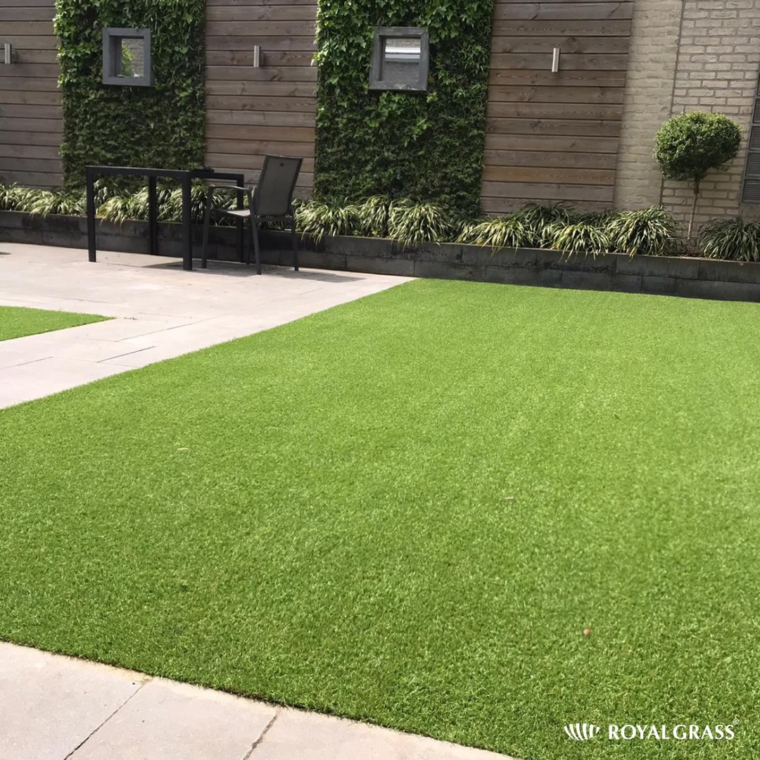 Nowoczesny ogród z równym trawnikiem, drewnianą ścianą z zielonymi pnączami, minimalistycznym zestawem mebli ogrodowych i kostką brukową