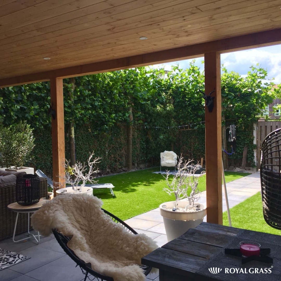 Zadaszony taras z drewnianą konstrukcją, sztuczną trawą w ogrodzie, meblami wypoczynkowymi i dekoracjami.