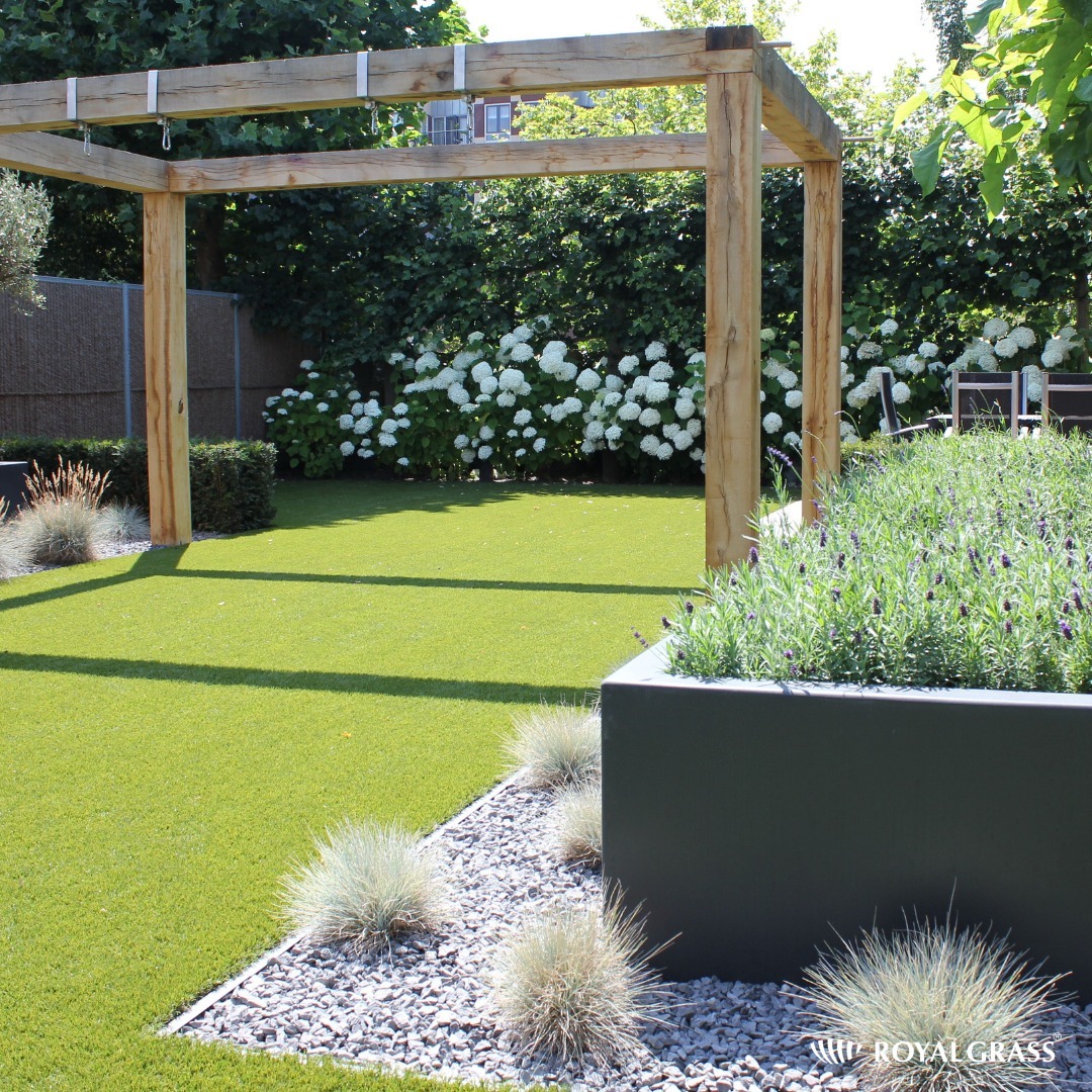 Nowoczesny ogród z drewnianą pergolą, sztuczną trawą, rabatą z lawendą w metalowej donicy i białymi hortensjami w tle.