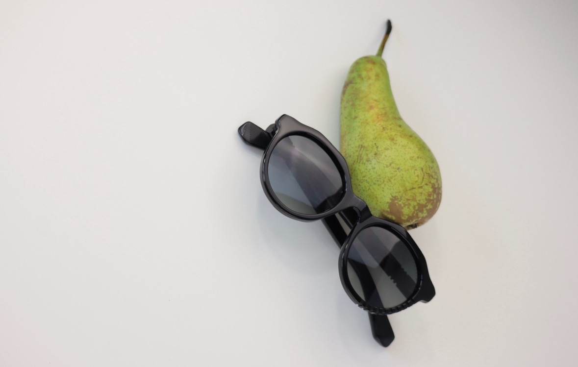 Para czarnych okularów przeciwsłonecznych leżąca obok zielonej gruszki na białym tle, ujęcie z góry.