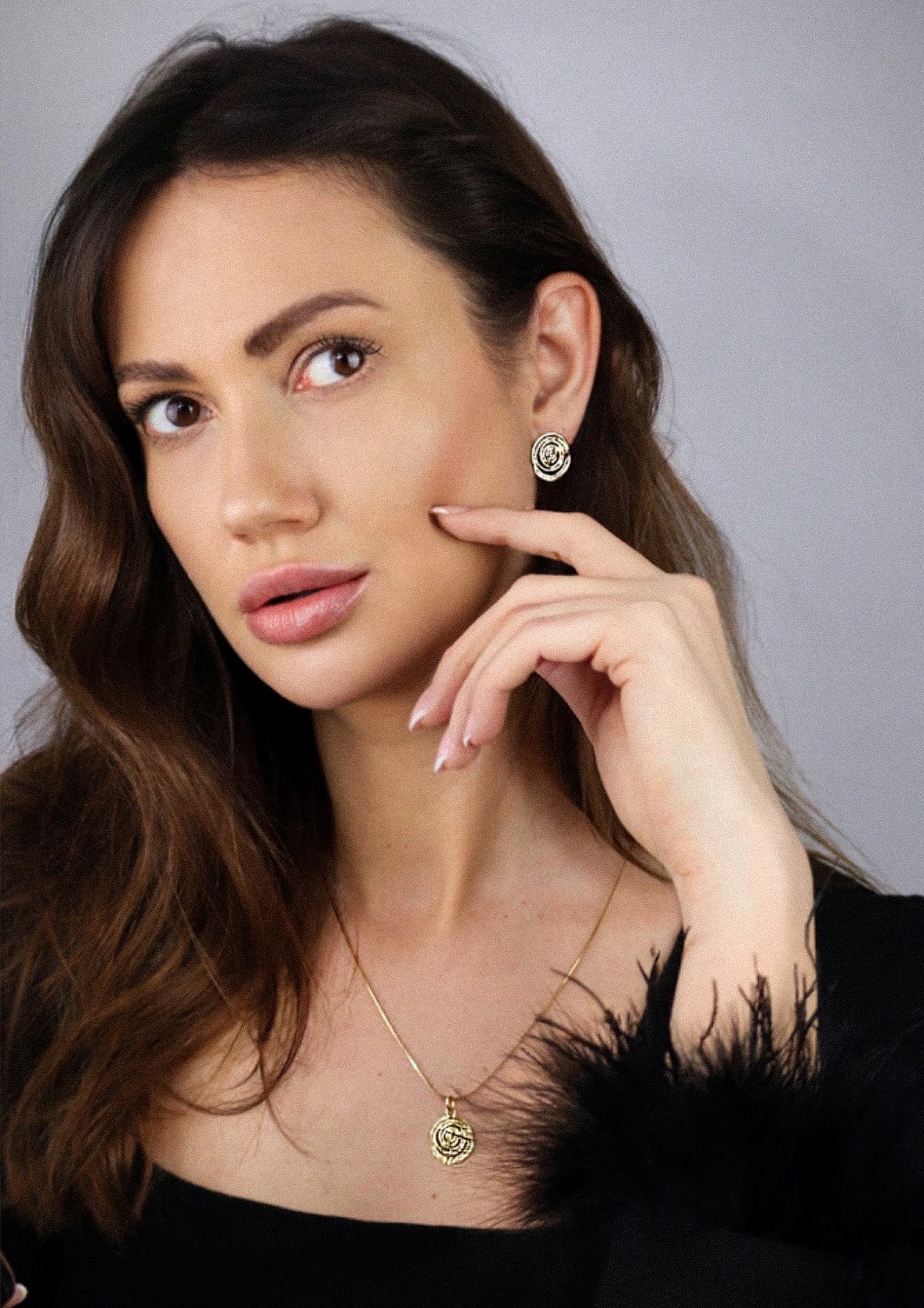 Portret kobiety w Poznaniu z delikatną biżuterią: złote kolczyki i naszyjnik z okrągłym wisiorkiem, czarna bluzka z piórami.