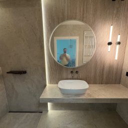 KD-BUD - Nowoczesna łazienka w beżowych tonacjach: okrągłe lustro z odbiciem osoby, umywalka nablatowa, dekoracyjne oświetlenie LED i ryflowana ściana.