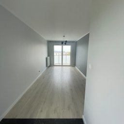 KD-BUD - Pomalowane na szaro i biało wnętrze z panelami podłogowymi, widok na balkon i logo firmy KD-BUD w rogu