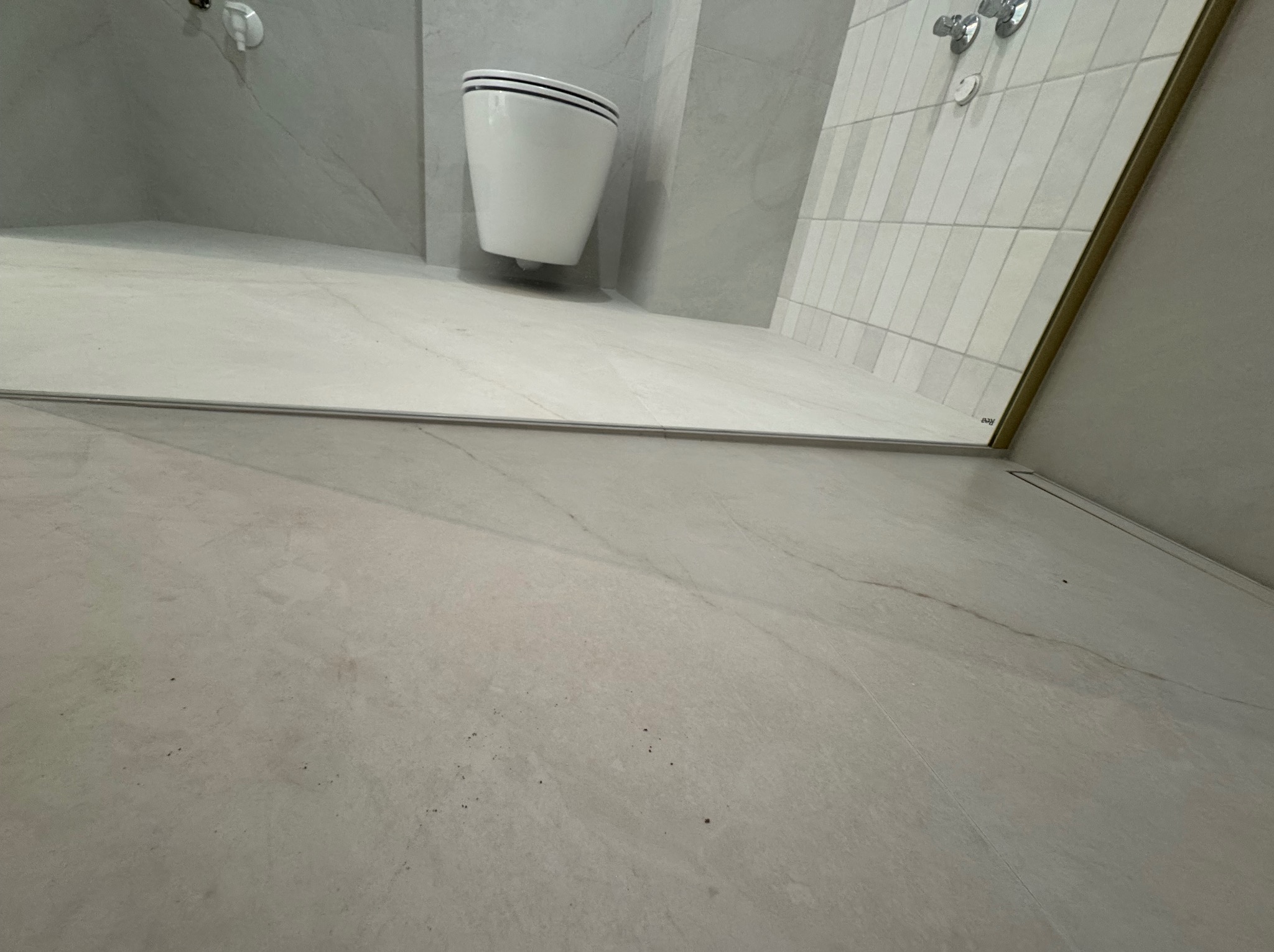 Nowoczesna łazienka z białymi płytkami imitującymi marmur na podłodze i ścianach. Wisząca toaleta z czarnymi akcentami. Minimalistyczny design.