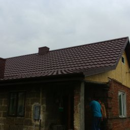 Usługi dekarsko-ciesielskie - Dom z brązowym dachem z blachodachówki, ceglanym kominem i częściowo otynkowaną elewacją, widoczne osoby przy wejściu.