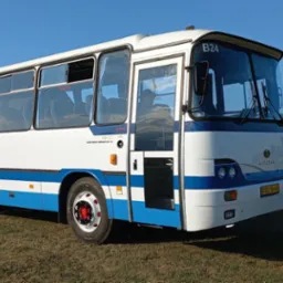 Biało-niebieski autobus Autosan H9-20 z otwartymi drzwiami, stojący na trawiastym terenie, z widocznym budynkiem w tle.