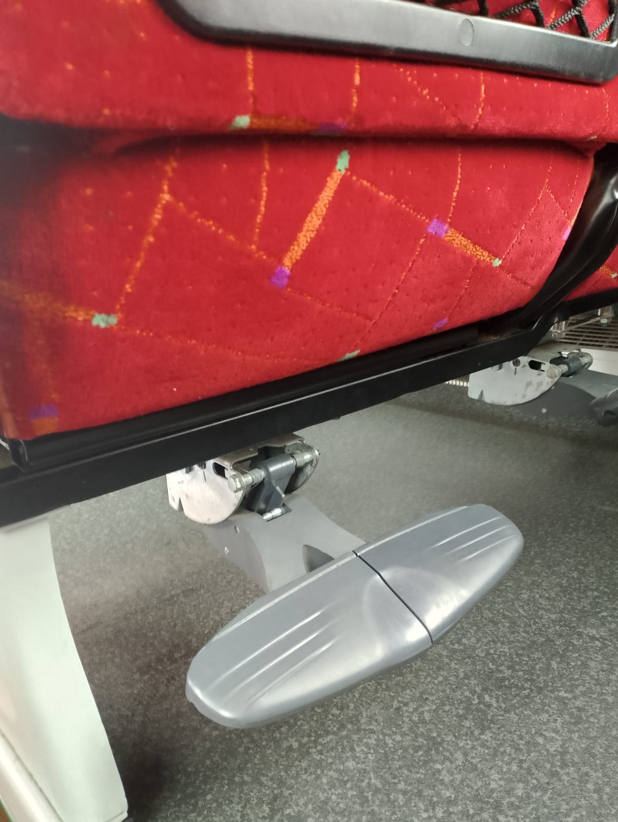 Czerwone, wzorzyste siedzenie z podnóżkiem w autobusie dalekobieżnym, widoczne z niskiego kąta.