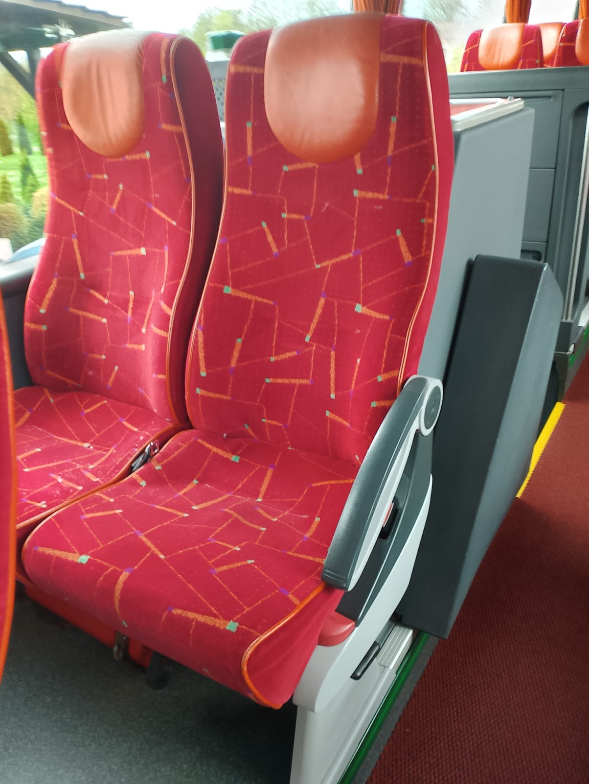 Czerwone, wzorzyste fotele pasażerskie w autobusie dalekobieżnym, z widocznym podłokietnikiem i zagłówkiem.