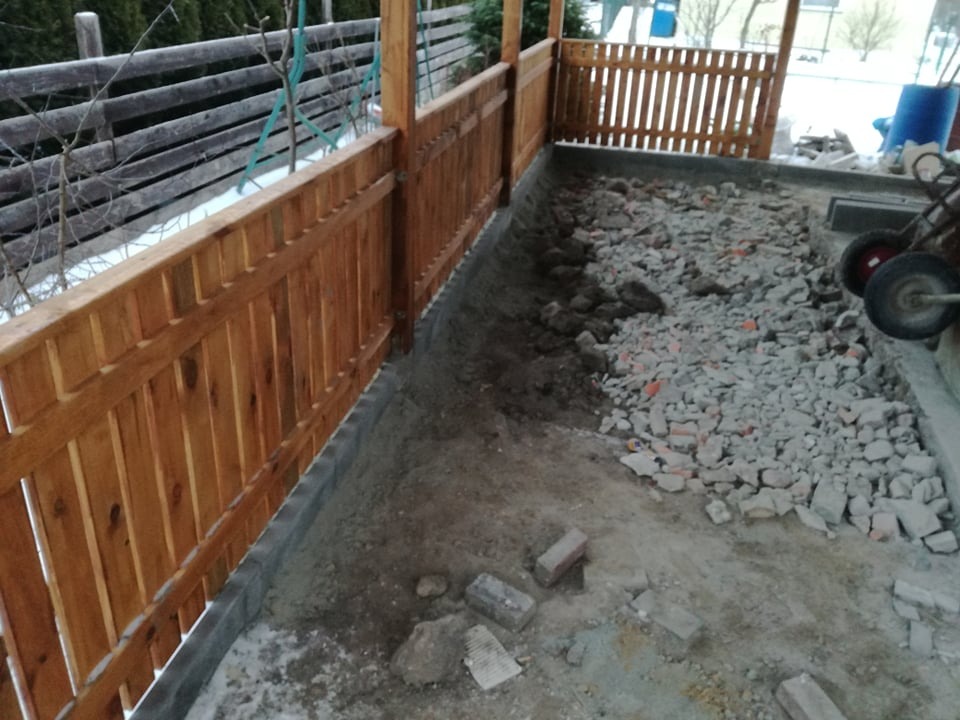 Przygotowanie podłoża pod taras z drewnianą balustradą, widoczne warstwy ziemi, gruzu i fundament z bloczków betonowych.