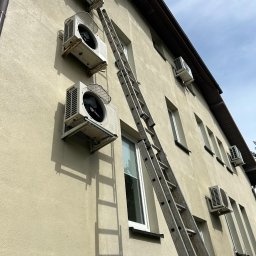 MGP Klimatyzacje - Montaż klimatyzacji na elewacji budynku. Widoczne jednostki zewnętrzne i drabina oparta o ścianę. Ujęcie z dołu podkreśla wysokość instalacji.