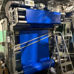 MGP Klimatyzacje - Montaż układu wentylacji przemysłowej z niebieskim filtrem w hali produkcyjnej w Warszawie. Widoczna drabina i pracownik w trakcie instalacji.