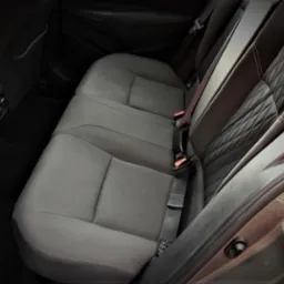 Wnętrze samochodu: tylna kanapa z trzema miejscami, szara tapicerka, pasy bezpieczeństwa z czerwonymi elementami, widoczne kratki wentylacyjne.