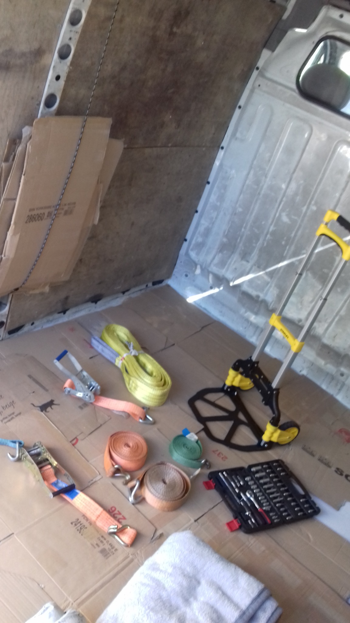 Wnętrze furgonetki wyłożone kartonem z pasami transportowymi, wózkiem transportowym Stanley i zestawem narzędzi.