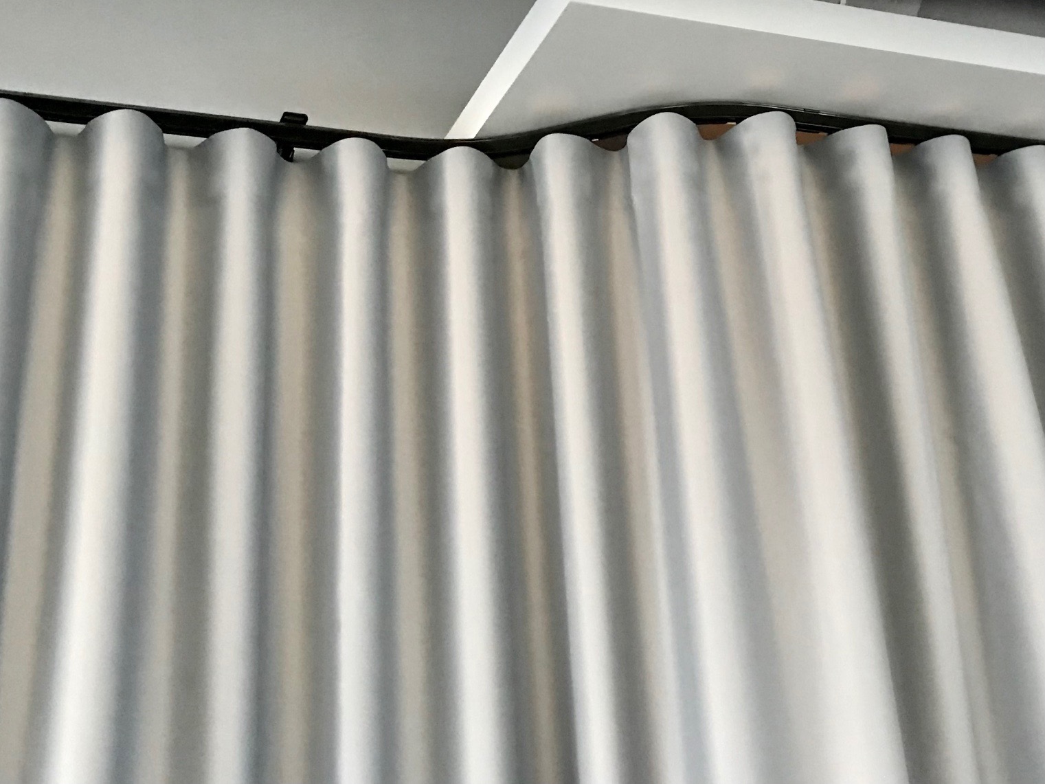 Delikatne, srebrzyste zasłony wave w eleganckim apartamencie w Warszawie, zawieszone na czarnym karniszu podsufitowym.