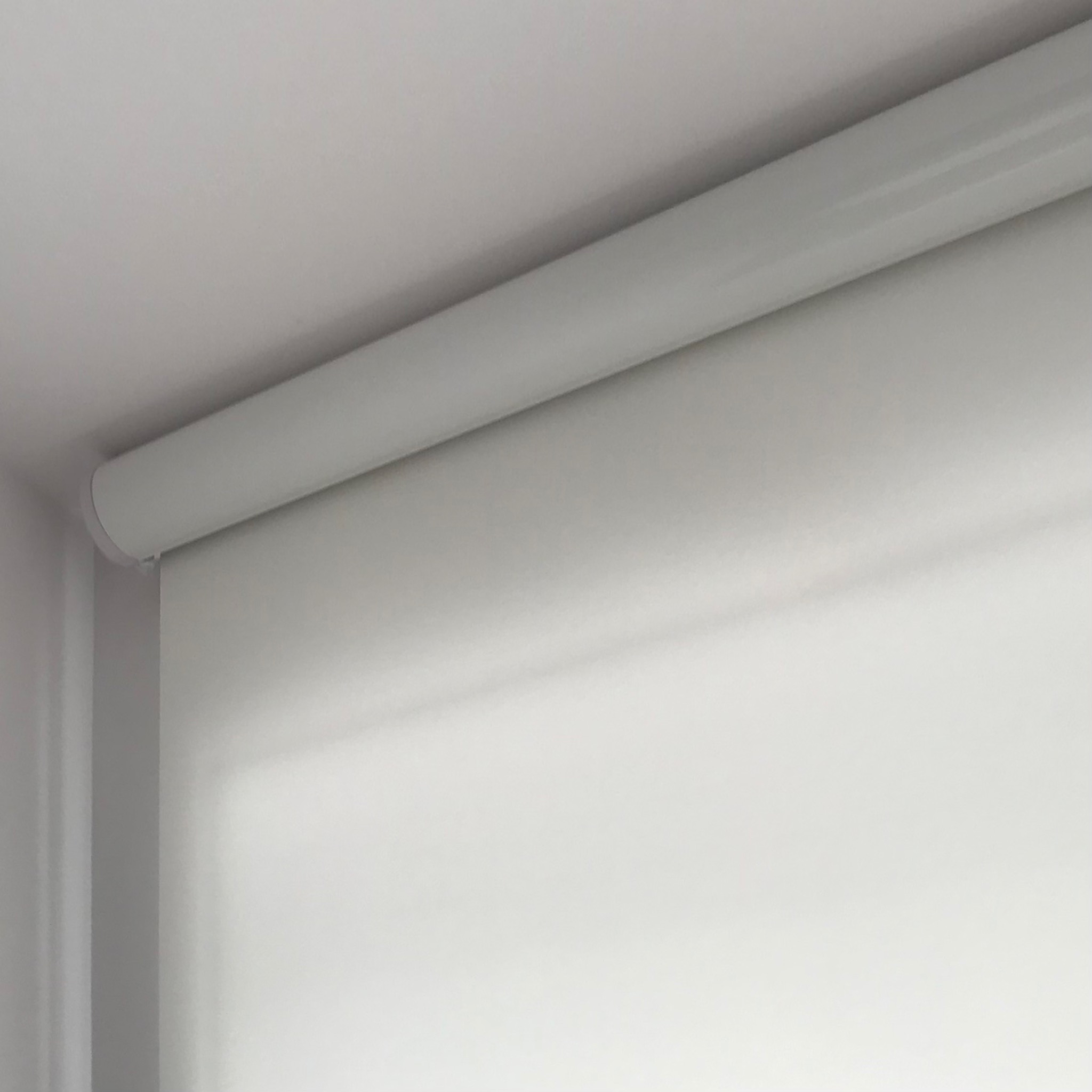 Minimalistyczna, biała roleta zwinięta u góry okna, widoczna z bliska, z delikatnym światłem dziennym.