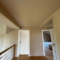 DEN-PRO Denys Demchuk - Beżowe wnętrze domu po malowaniu: ściany, sufit, białe drzwi i drewniana podłoga. Widok na pokój z łóżkiem przez otwarte drzwi. Minimalistyczny styl.