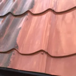 Częściowo oczyszczony dach z metalowej dachówki w kolorze miedzianym, widoczna różnica między brudną a umytą powierzchnią.