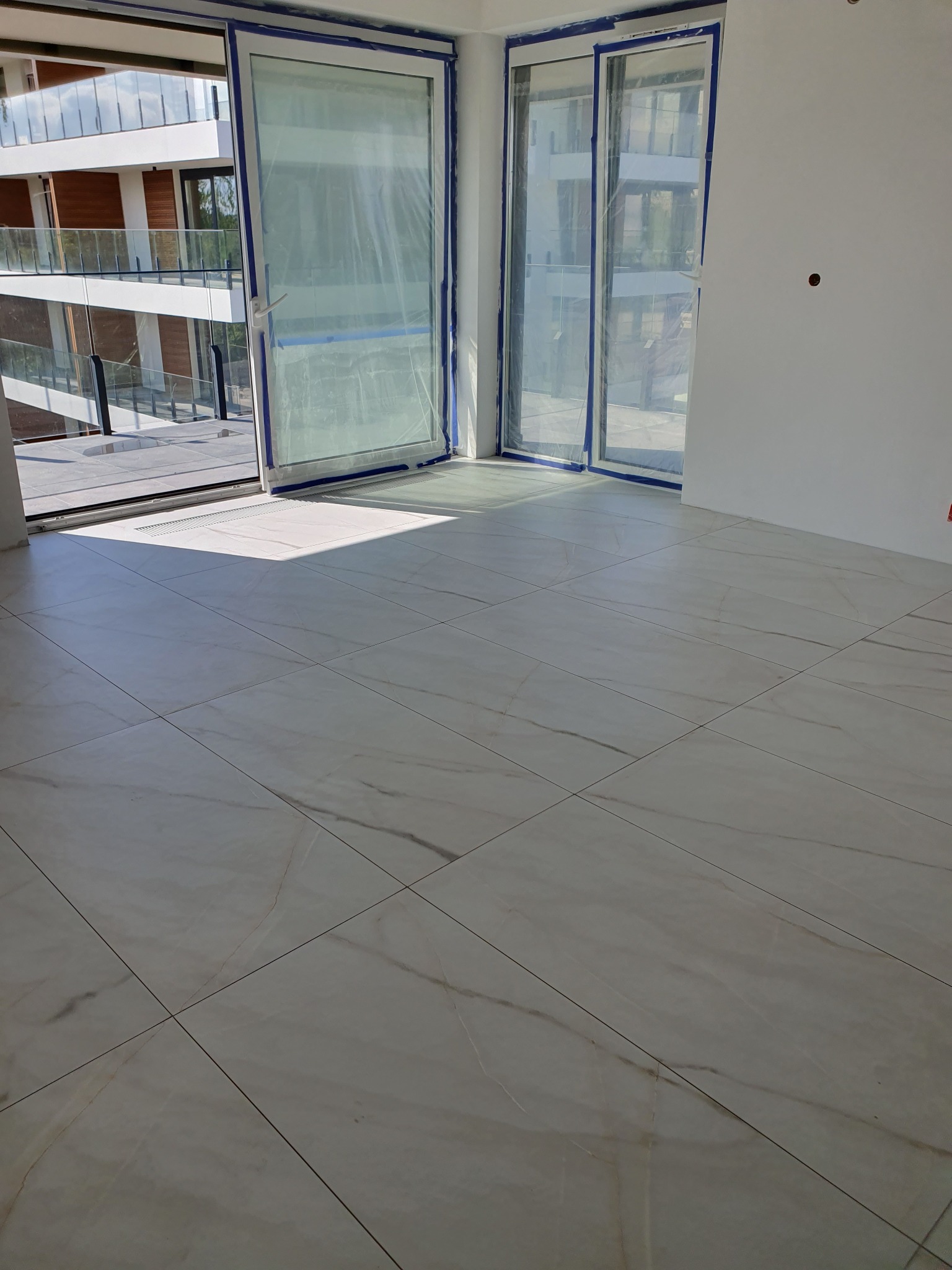 Ułożona, jasna, marmurowa podłoga w nowym apartamencie z zabezpieczonymi folią oknami balkonowymi i surowymi ścianami.