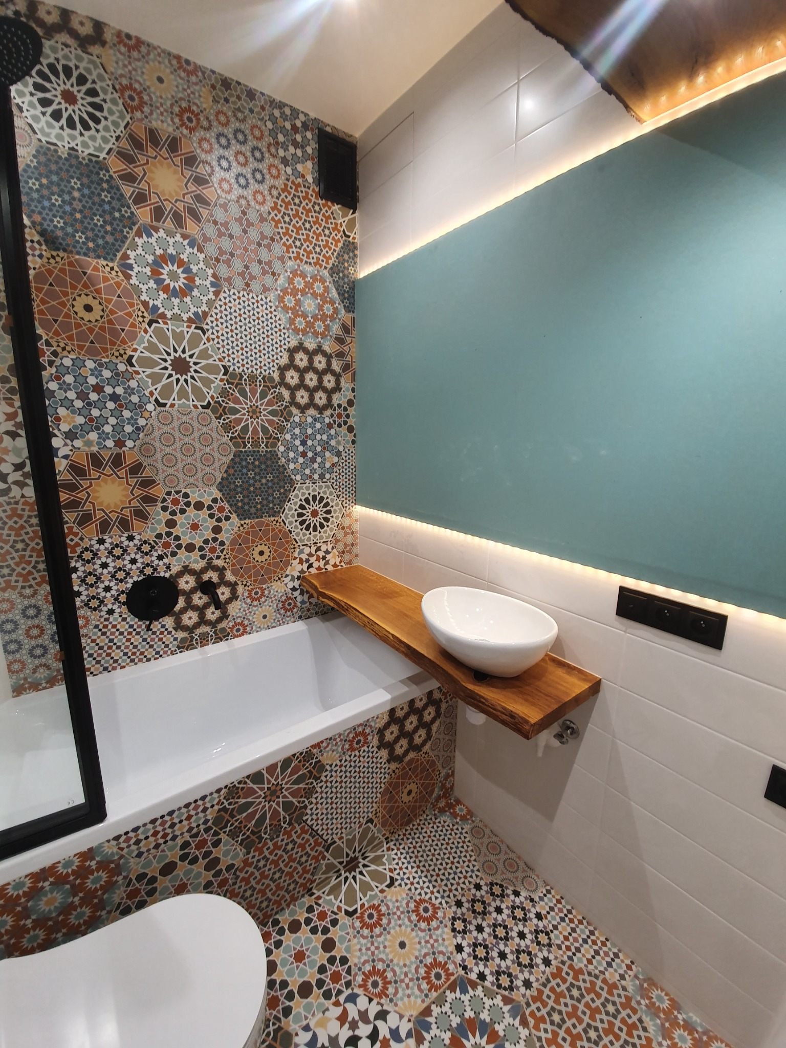Nowoczesna łazienka z wanną, umywalką nablatową na drewnianym blacie i heksagonalnymi płytkami w stylu marokańskim na ścianach i podłodze, podświetlane lustro.
