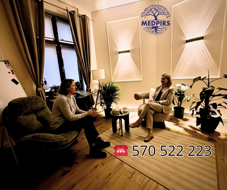 Dwie kobiety w jasnym gabinecie podczas rozmowy, otoczone roślinami. Na ścianie dekoracyjne lampy i logo Medpirs. W tle okno z zasłonami i biurko.