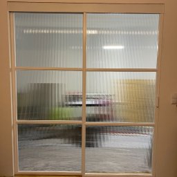 AP Welding Concept - Segment drzwi przesuwnych z białymi profilami i szybą hartowaną typu flutes, widoczne obustronne domykanie firmy GEZE.