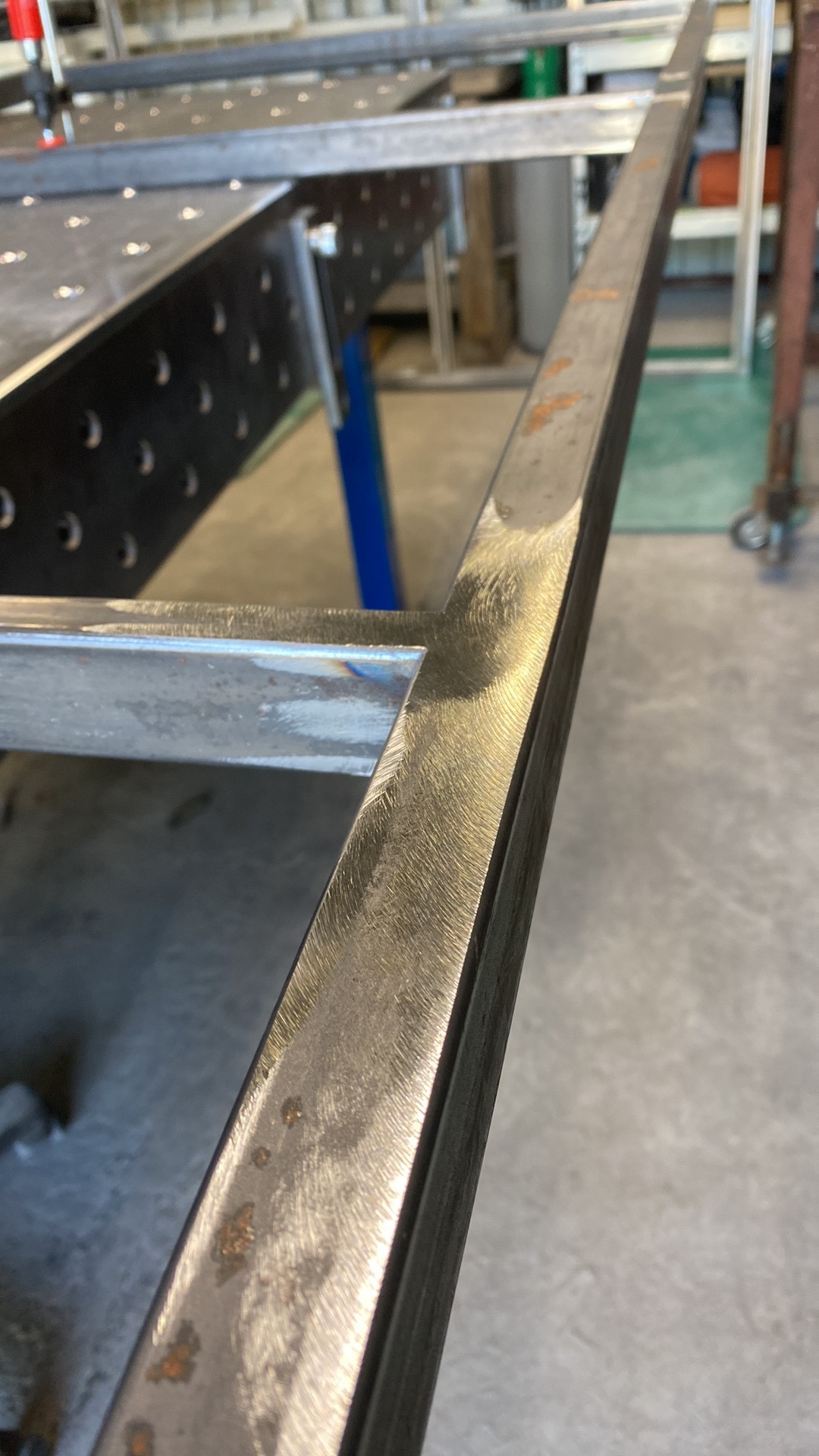 Detale spawania metalowej ramy na stole spawalniczym, widoczne ślady obróbki i spawania, narożnik ramy z wyraźnym łączeniem.