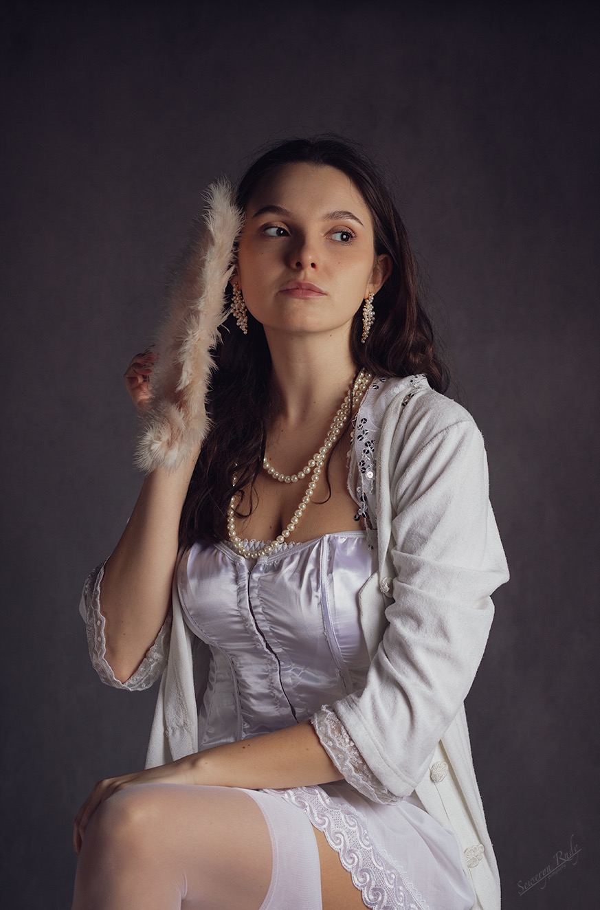 Portret kobiety w białym gorsecie i perłach, trzymającej wachlarz z piór na ciemnoszarym tle.