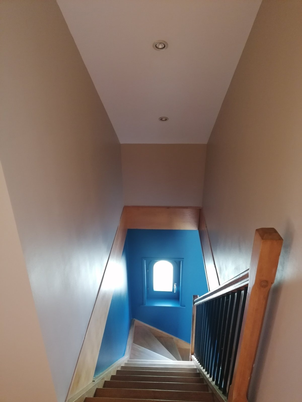 Klatka schodowa po malowaniu z błękitną ścianą z oknem i drewnianymi schodami, widok z góry.