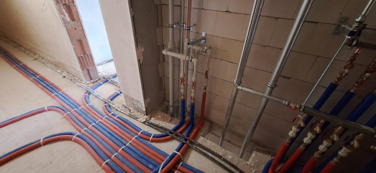 Rozłożone rury ogrzewania podłogowego w kolorze niebieskim i czerwonym. Instalacja przed wylaniem posadzki, widoczne mocowania i elementy montażowe.